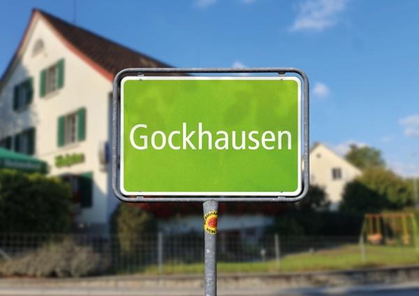Symbolbild: ein grünes Ortseingangsschild mit der Aufschrift "Gockhausen". Im Hintergrund ist der Frohsinn zu sehen. (Artischock)